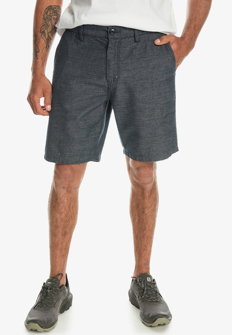 Herrshorts i mörkgrått i en texturerad tyg, med knappstängning, bältesöglor och sidofickor. Bärs med grå sportskor.