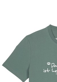 Mouw en schouder van een gedempte groene T-shirt met gedeeltelijke witte tekst in het Duits, beginnend met "Das ist".