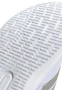 Hvid sneakersål med tekstureret grebmønster, der har ribbede sektioner og en glat, let hævet kant. Accenter i lysegrå.