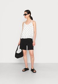 Camisola com padrão floral branco, calções pretos, bolsa preta e sandálias. Tecido suave, corte solto, design simples e detalhes minimalistas.