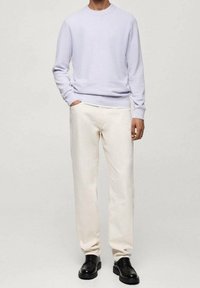 Pull violet clair à col rond associé à un pantalon écru et des chaussures noires à lacets. Texture lisse, coupe décontractée et palette de couleurs neutres.