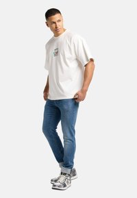Hvid bomulds t-shirt med en diskret blomstergrafik på brystet, parret med slim-fit blå jeans og mønstrede høj-top sneakers.
