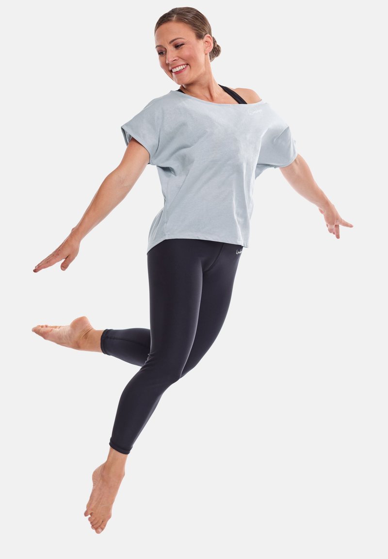 Light blue oversized t-shirt with short sleeves paired with black fitted leggings. Model is in a dynamic pose, barefoot.