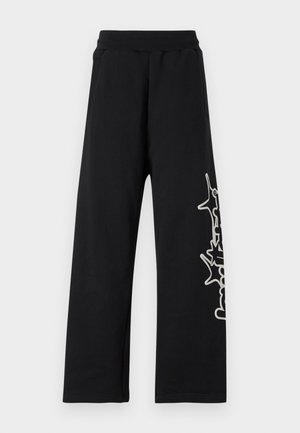 Schwarze Jogginghose mit weitem Bein, elastischem Bund, seitlichen Taschen und einem weißen Grafikdesign entlang des linken Beins. Hergestellt aus weichem Stoff.