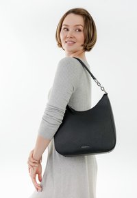 Schwarze Handtasche mit strukturierter Oberfläche und geschwungener Form, ausgestattet mit einem silbernen Kettenriemen. Die Tasche wird über der Schulter getragen gezeigt.