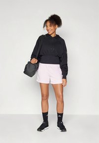 Μαύρο φούτερ με κουκούλα, ανοιχτό ροζ σορτς, μαύρες αθλητικές κάλτσες και μαύρα αθλητικά παπούτσια. Κρατάει μια μικρή μαύρη τσάντα. Απλή, καθημερινή αθλητική εμφάνιση.