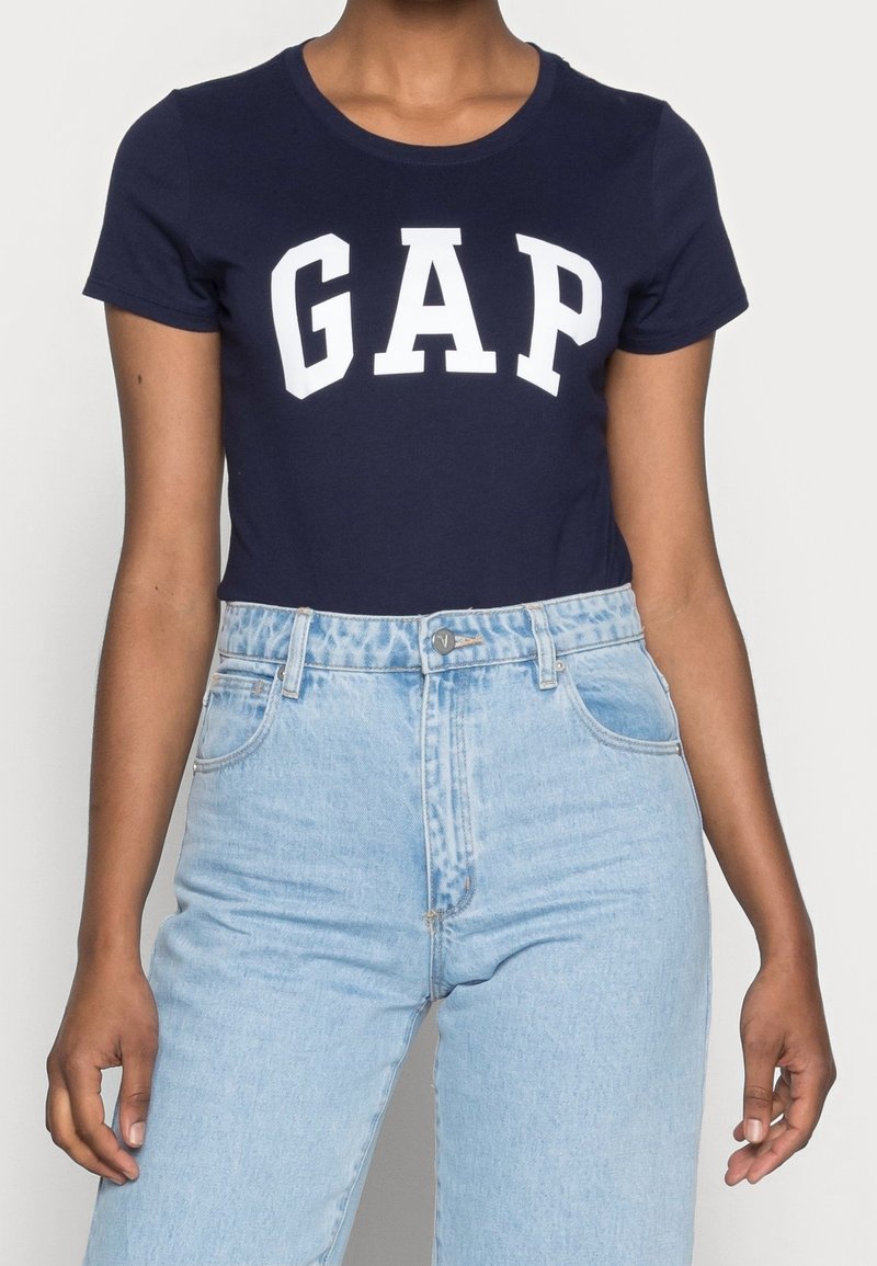 Mörkblå t-shirt med kort ärm och vit "GAP" logga; kombinerad med ljusblå högmidjade jeans som har knappstängning och fickdetaljer.