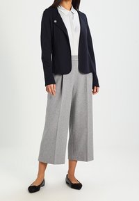 Laivastonsininen bleiseri kauluksineen, harmaat leveälahkeiset housut ja mustat balleriinat. Valkoinen kauluspaita alla. Pinta on sileää kangasta, ei näkyviä kuvioita.