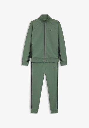 Groen trainingspak gemaakt van soepel stof, bestaande uit een jas met ritssluiting met zwarte strepen en een bijpassende broek; strak ontwerp met geribbelde manchetten.