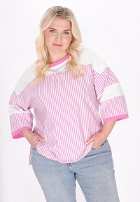 Rosa och vit randig oversized skjorta med korta ärmar, rund halsringning och kontrasterande kant. Bärs med ljusblå jeans.