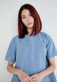Gai zila džinsa blūze ar īsām piedurknēm, strukturētām šuvēm un brīvu piegriezumu. Iespējas plaša kakla izgriezums un smalks raksts.
