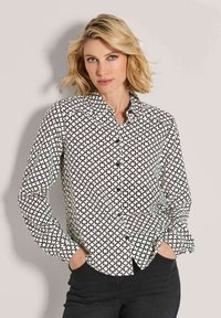 Black and white button-up shirt with a geometric pattern, featuring a pointed collar and long sleeves, shown paired with dark jeans.