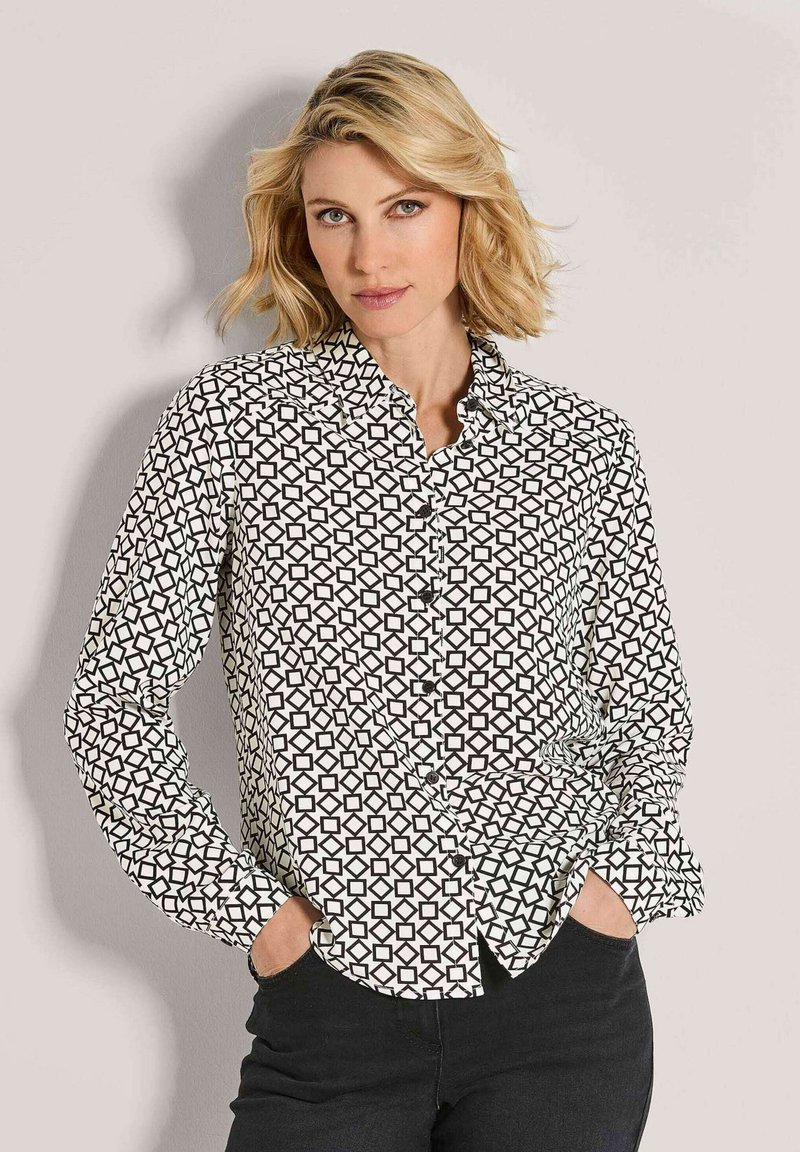 Black and white button-up shirt with a geometric pattern, featuring a pointed collar and long sleeves, shown paired with dark jeans.