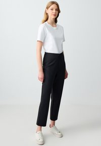 T-shirt blanc à manches courtes associé à un pantalon noir taille haute, présentant un design épuré et une texture lisse. Porté avec des baskets blanches.