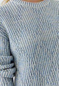Gebreide trui met horizontale blauwe en witte strepen, voorzien van een geribde halslijn en een gestructureerde stof. Zacht, casual ontwerp met opgerolde mouwen.