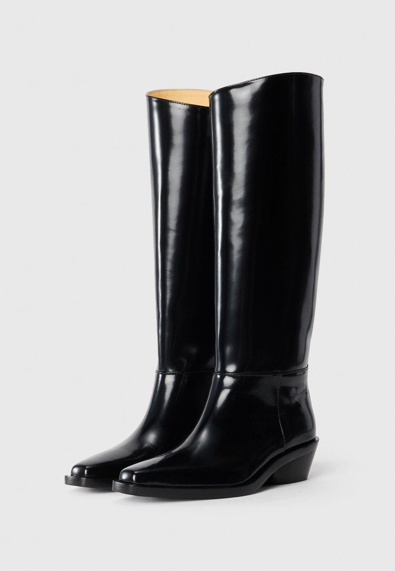 Hohe schwarze Lederstiefel mit spitzen Zehen und niedrigem, schrägem Absatz, die nebeneinander auf einem schlichten weißen Hintergrund stehen.