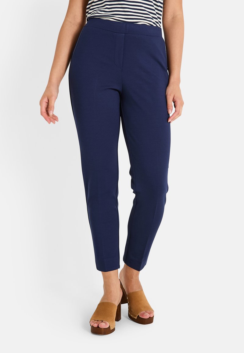 Pantalones de stretch azul marino con una forma ajustada, cinturilla elástica y un sutil detalle en las costuras laterales, combinados con sandalias de plataforma en color tostado.