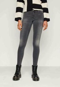 Jeans skinny cinzentos com um acabamento desbotado, apresentando cinco bolsos e passagens para cinto, combinados com botas pretas de atacador. Suéter listrado por cima.