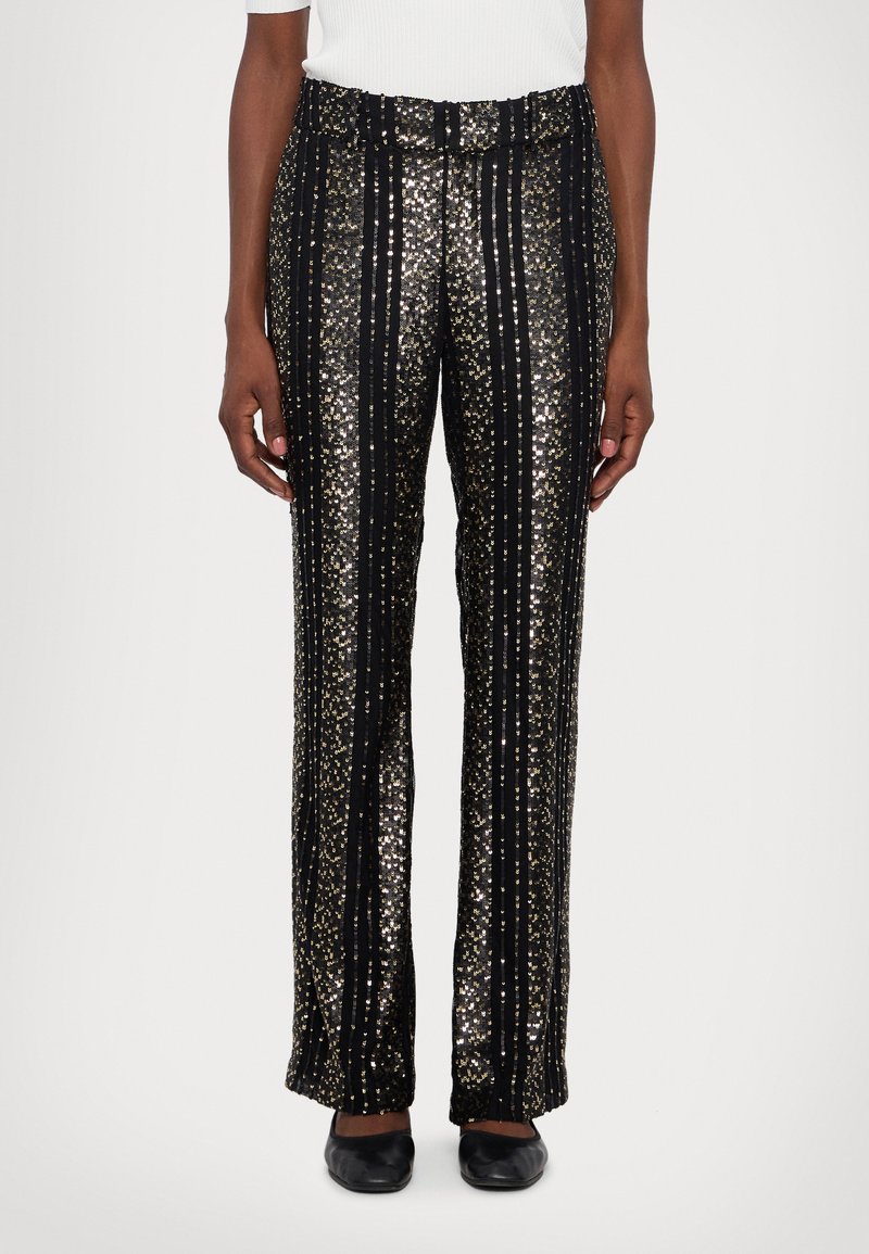 Black sequin pants with vertical gold stripes, featuring a loose fit, elastic waistband, and smooth texture. Worn with black flats.