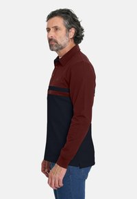 Camisa polo de manga larga en rojo y navy con cuello, rayas horizontales en contraste y aberturas laterales en el dobladillo.