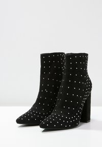 Schwarze Wildleder-Stiefeletten mit spitzer Zehenpartie und klobigem Absatz, versehen mit silbernen Nieten in einem verstreuten Muster.