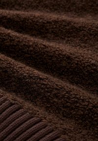 Bruine gestructureerde stof met dikke, zachte vezels en een geribbelde sectie. Benadrukt verschillende texturen en een rijke, diepe kleur.