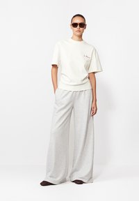 Biała koszulka z krótkim rękawem z czerwonym haftowanym napisem, w połączeniu z jasnoszarymi szerokimi spodniami dresowymi i ciemnobrązowymi butami. Noszone ciemne okulary przeciwsłoneczne.