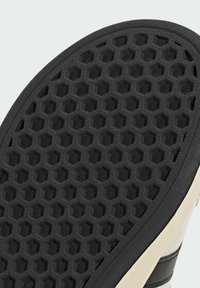 Zwarte rubberen schoenzool met een hexagonaal patroon, een gestructureerd oppervlak en een crèmekleurige rand met een gemarkeerde omtrek.