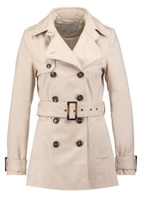 Trench-coat beige à double boutonnage, larges boutons noirs, taille cintrée avec ceinture et épaulettes. Col classique.