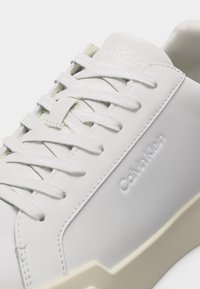 Λευκό αθλητικό παπούτσι Calvin Klein με λευκά κορδόνια, διακριτικό ανάγλυφο λογότυπο στο πλάι και σόλα κρεμ χρώματος.