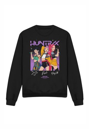 Black sweatshirt with colorful cartoon of three female K-pop characters holding microphones under the word "HUNTRX" in purple.
