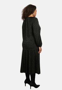 Abito nero con una discreta stampa verde, maniche lunghe, dettaglio arricciato sul retro e una gonna fluida. Indossato con stivali neri fino al ginocchio.