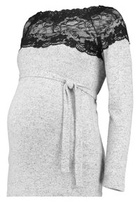 Robe de maternité grise à manches longues, avec un empiècement en dentelle noire au niveau du décolleté et un détail de taille nouée. Tissu doux et texturé.