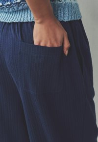 Pantaloni cu dungi bleumarin, dintr-un material texturat, cu o buzunar lateral. Talia este elastică, oferind confort și ușurință în purtare.