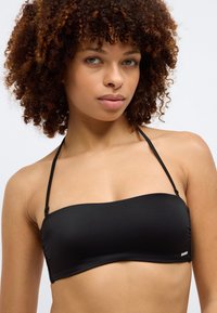 Μαύρο μπαντέο μπικίνι τοπ με λεπτές ρυθμιζόμενες τιράντες, λεία υφή, διακριτική πτυχή στο πλάι και μικρή λεπτομέρεια λογότυπου στο πλάι.