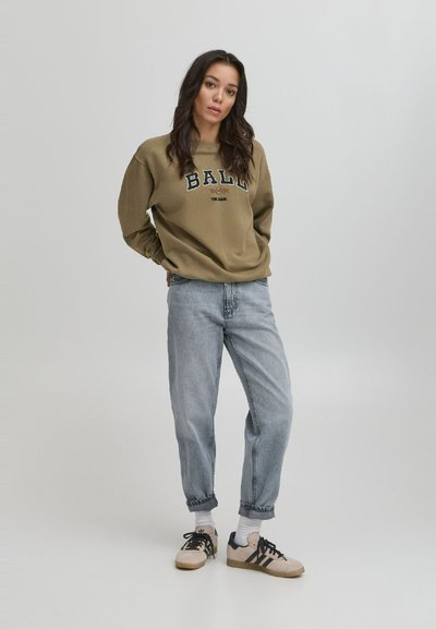 Felpa verde oliva con logo "BALL", abbinata a jeans azzurri. Indossata con sneakers nere e marroni, completate da calzini bianchi.