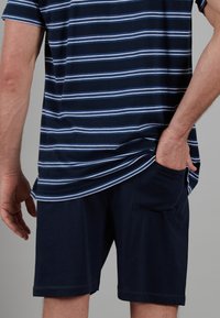 Marine gestreiftes T-Shirt mit blauen und weißen Streifen, kombiniert mit einfarbigen marineblauen Shorts mit einer Seitentasche. Weiches Baumwollmaterial, lässige Passform.