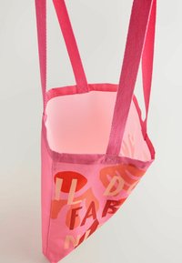 Pink fabric tote bag with matching pink straps, featuring abstract red and orange shapes and partially visible text on the front.