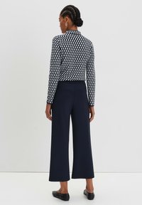 Top a maniche lunghe con un motivo geometrico in blu navy e bianco, abbinato a pantaloni a gamba larga blu navy a vita alta. Tessuto morbido e design aderente.