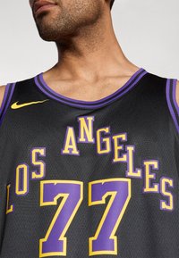 Camisa de basquetebol preta com detalhes em roxo, "LOS ANGELES" e "77" em texto negrito amarelo e roxo. Logótipo da Nike em amarelo no ombro.