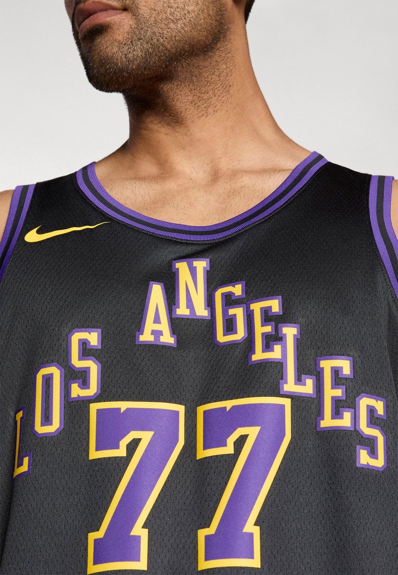 Camisa de baloncesto negra con detalles en púrpura, "LOS ÁNGELES" y "77" en texto amarillo y púrpura en negrita. Logotipo de Nike en amarillo en el hombro.