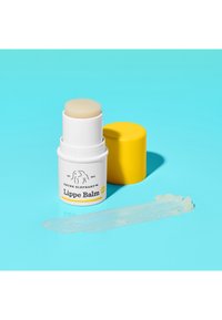 Lippenbalsam in einem weißen zylindrischen Behälter mit gelbem Deckel. Klarer Balsamstick oben, mit einem Strich des Balsams auf blauem Hintergrund.