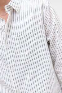 Nærbilde av en person som har på seg en hvit skjorte med knapper, med tynne vertikale svarte striper og en brystlomme på venstre side.