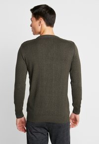 Olivgrüner Strickpullover mit Fischgrätenmuster, geripptem Rundhalsausschnitt und Bündchen. Mit langen Ärmeln und figurnaher Silhouette.