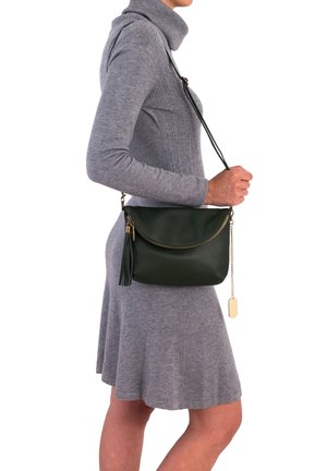 Dunkelgrünes Leder-Crossbody-Tasche mit abgerundeter Form, goldener Reißverschluss, Quastenakzent und Metallschild-Detail. Getragen mit einem grauen gerippten Kleid.