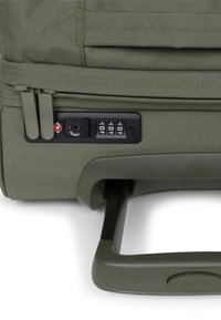 Valigia verde oliva con tessuto strutturato, due cursori grigi per la zip, un meccanismo di blocco conforme TSA e una maniglia retrattile.