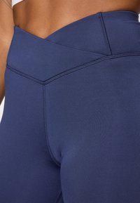 Legginguri înalțe de culoare albastru marin, cu un design fără cusături și detaliu încrucișat la talie, dintr-un material elastic.