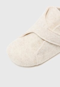Ulltofflor i off-white med en mjuk, strukturerad yta. Har en överlappande design för enkel påtagning och en rund tåform.