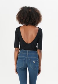 Top nero a maniche corte con scollatura profonda sulla schiena, abbinato a jeans in denim blu a vita alta con tasche posteriori e dettagli di branding discreti.
