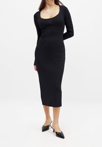 Robe midi noire côtelée à manches longues et décolleté carré, silhouette ajustée, associée à des mules à talons noires et bouts pointus.